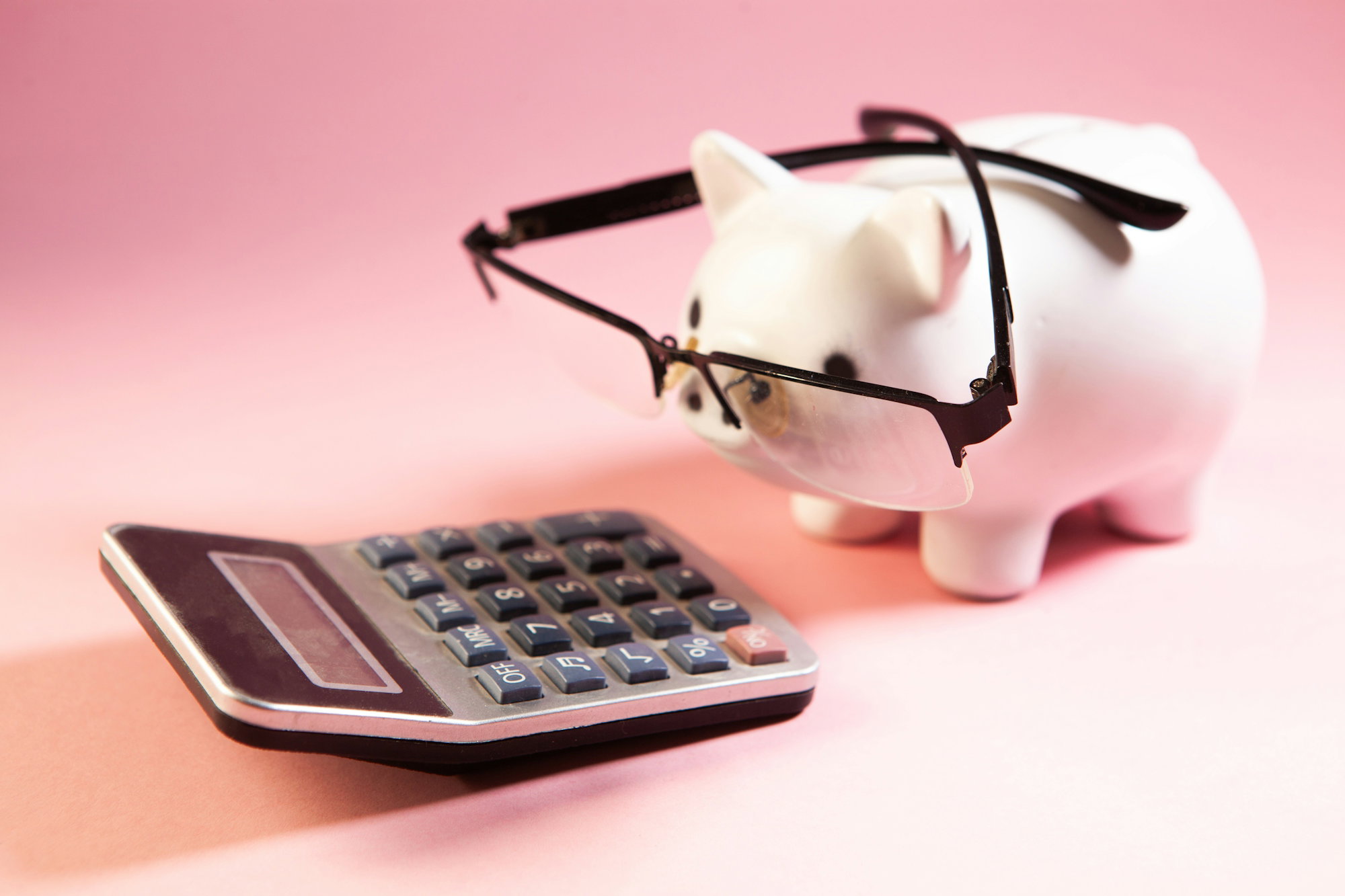 a-piggy-bank-wearing-glasses-next-to-a-calculator-.jpg A piggy bank wearing glasses next to a calculator.